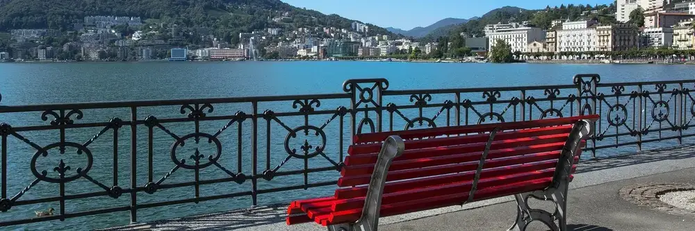 Red bench overlooking Lake Lugano and the cityscape – symbolising stability, reflection and personalised wealth management by FF Marcuard SA in Switzerland. Red bench overlooking Lake Lugano and the cityscape – symbolising stability, reflection and personalised wealth management by FF Marcuard SA in Switzerland.